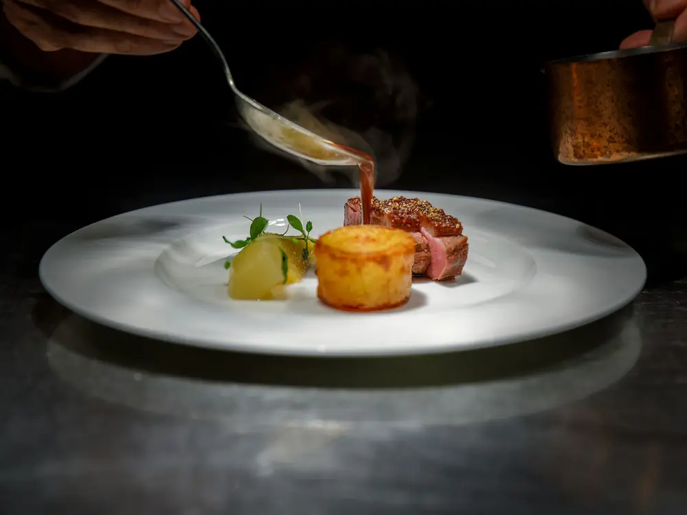 O chef termina um prato do menu degustação com o molho