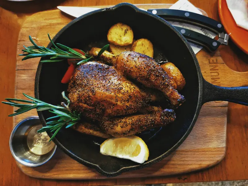 Frango assado dourado numa frigideira de ferro com batatas, alecrim e limão