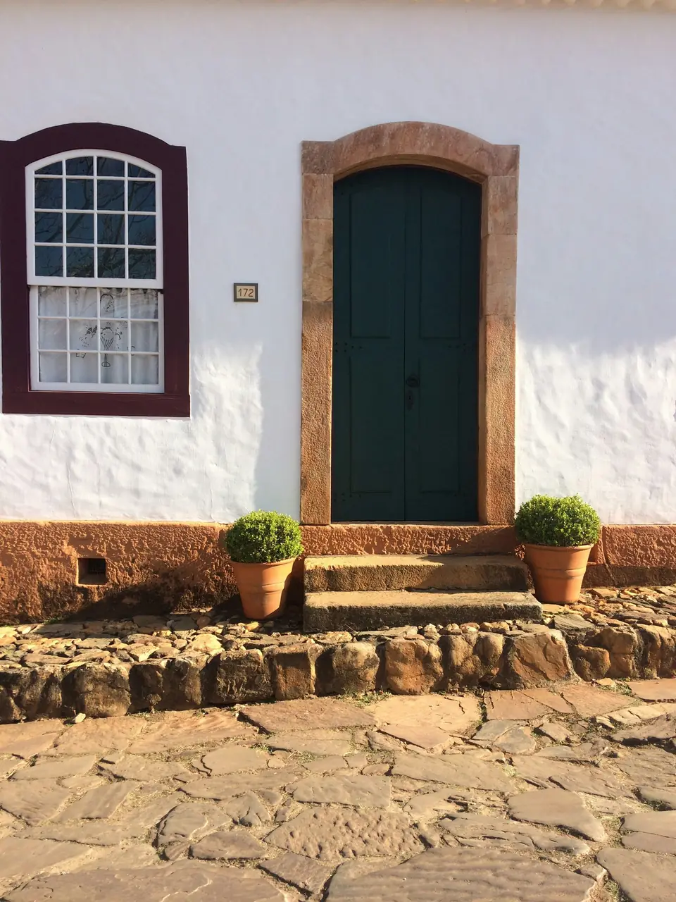 A entrada da casa: parede caiada, janela sangue-de-boi e porta verde
