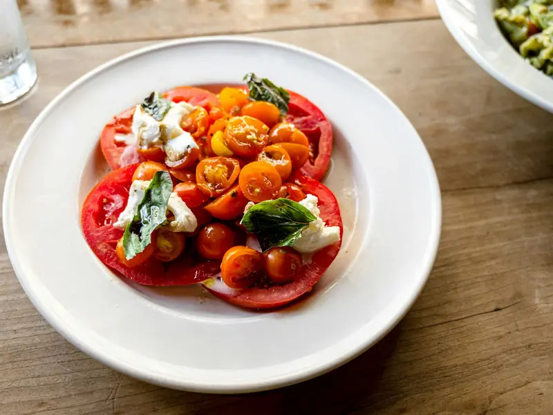 Prato de tomates coloridos fatiados com queijo branco e folhas